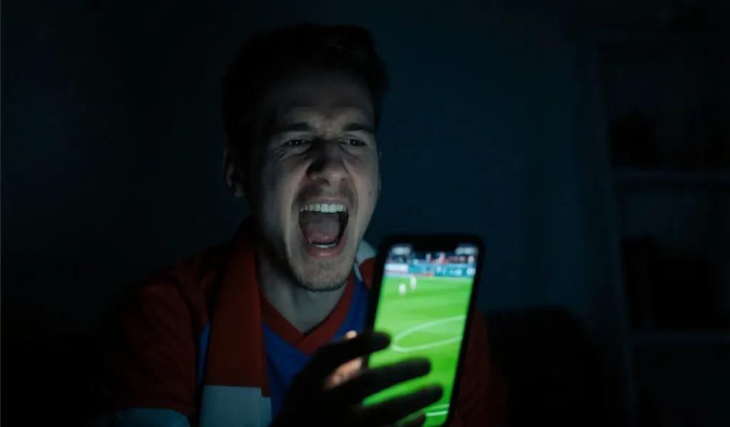 深夜在微弱灯光下用手机观看足球比赛直播的球迷，神情专注
